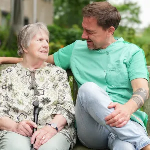 Zorgmedewerker samen met cliënt op een bankje in de tuin 